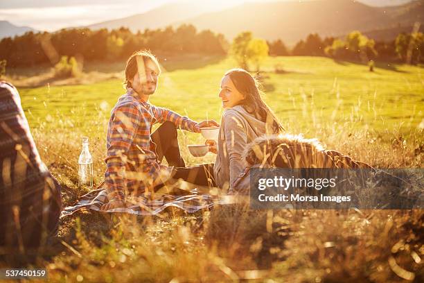 happy couple holding bowls on field - picnic stock-fotos und bilder