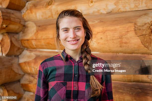 happy young woman standing against log cabin - chemise à carreaux photos et images de collection