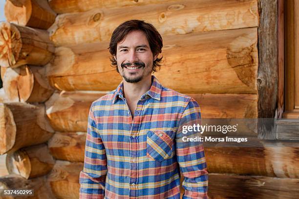 happy man standing against log cabin - flannel shirt stock pictures, royalty-free photos & images