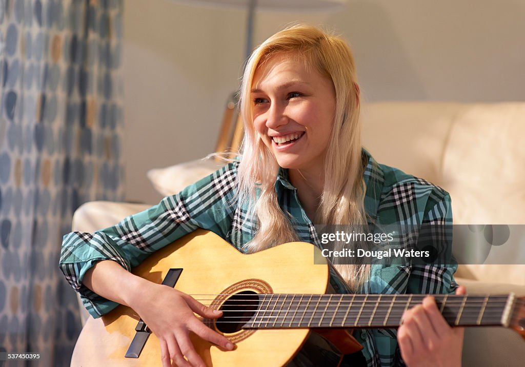 Woman playing guitar and smiling at home.