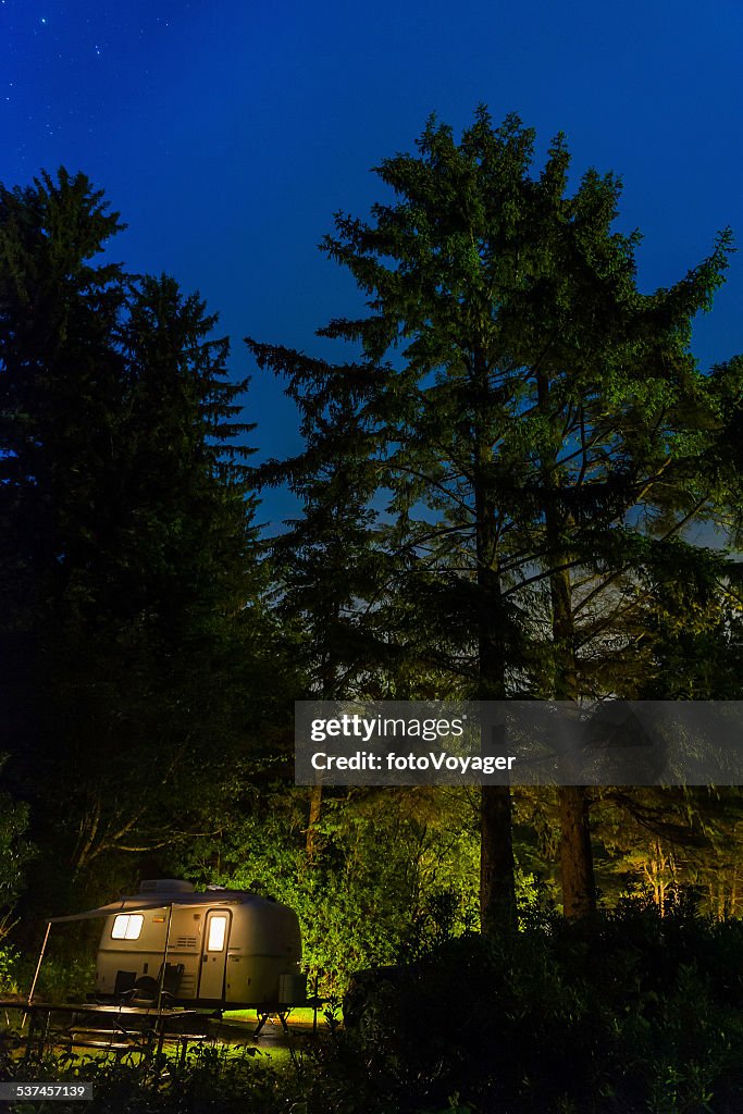 Stars shining over illuminated trailer forest campsite Pacific Northwest USA