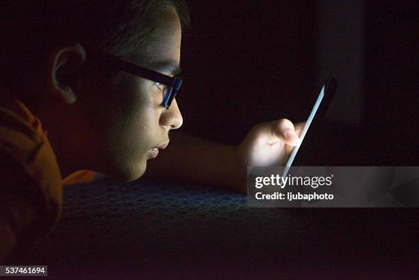 teenager sending email from smart phone in his bed - cyberbullying stock pictures, royalty-free photos & images