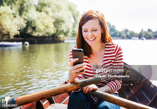 woman with smart phone in row boat. - rowboat stock pictures, royalty-free photos & images