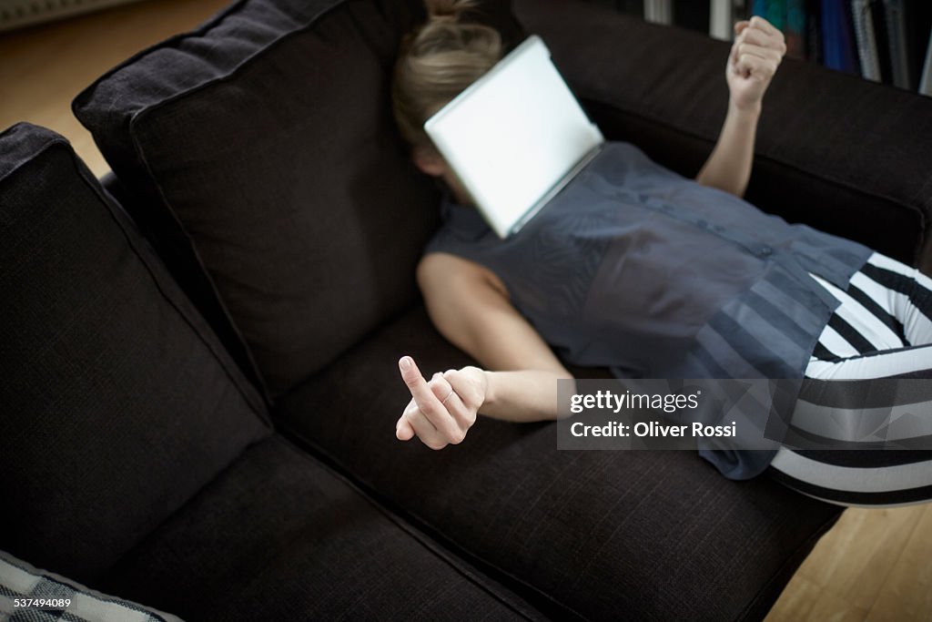 Playful young woman on couch with digital tablet