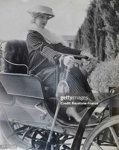 Bette Davis, on a film set, wearing a 1900 dress, poses aboard a car in the United States, circa 1930.