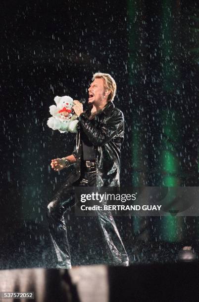 Le chanteur de rock et acteur français Johnny Hallyday chante avec un ours en peluche à la main, le 11 septembre 1998 sur la scène du Stade de France...