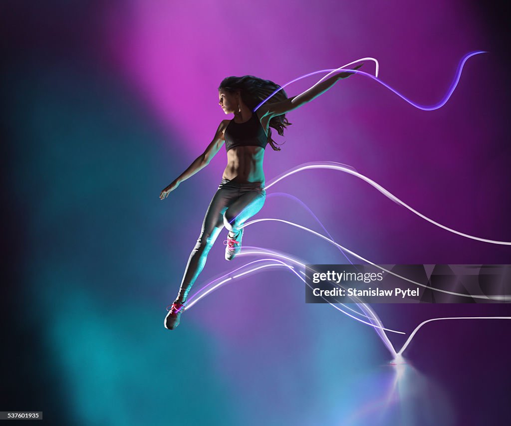 Female athlete jumping, leaving streaks of light
