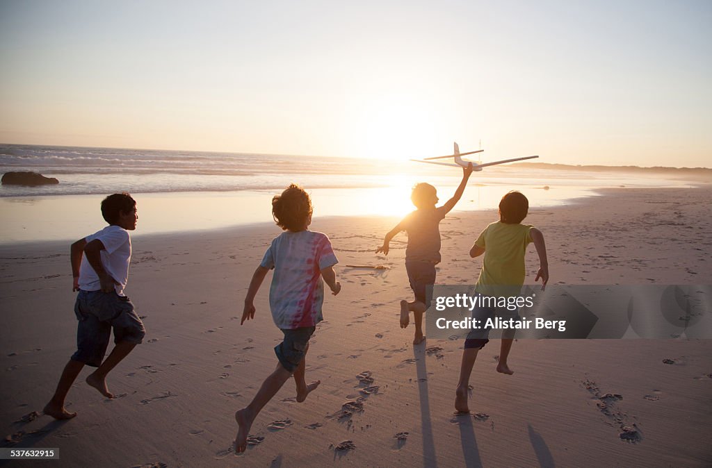 Boys running along beach with a toy plane