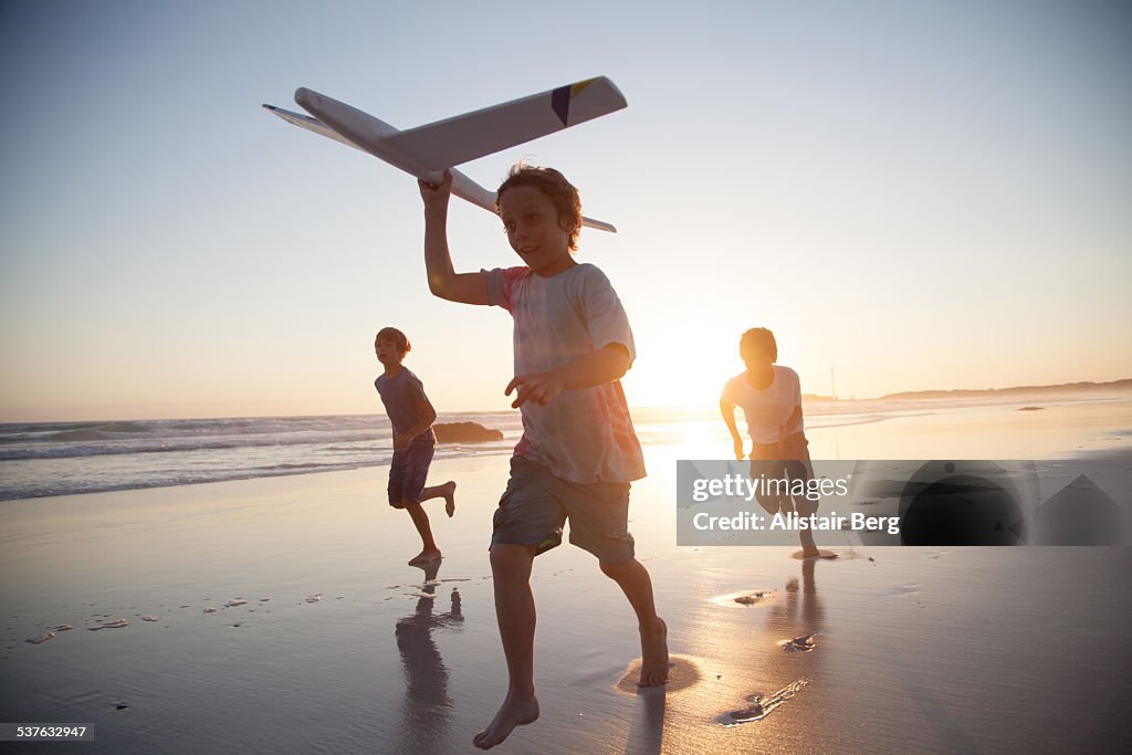 Boys running along beach with a toy plane