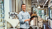Smiling brewmaster using tablet in factory