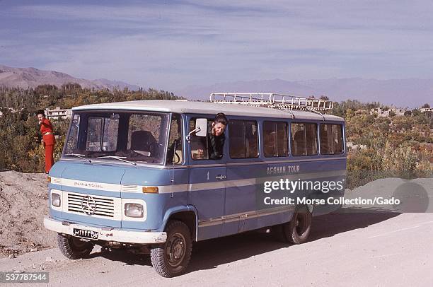 Blue Mercedes mini bus marked "Afghan Tour" with Western women at a pit stop on a dirt road outside of Kabul, Afghanistan. November, 1973. .