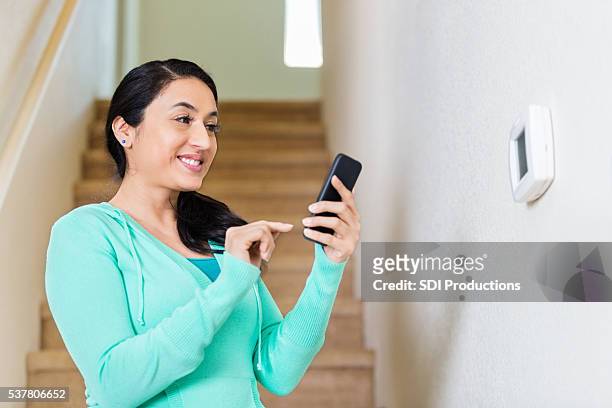 hispanic woman adjusts thermostat with smart phone - adjusting bildbanksfoton och bilder