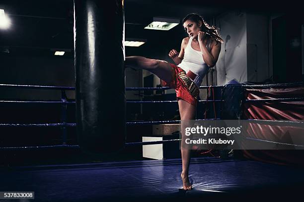 hembra muay thai de entrenamiento de combate con una bolsa de boxeo - muay thai fotografías e imágenes de stock