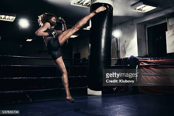 kickboxer hembra capacitación con una bolsa de boxeo - kick boxing fotografías e imágenes de stock