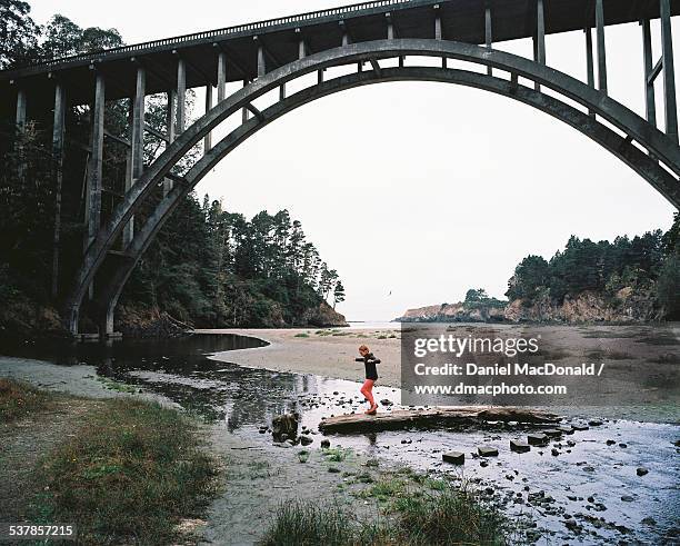 young girl crossing creek at beach under bridge - mendocino bildbanksfoton och bilder