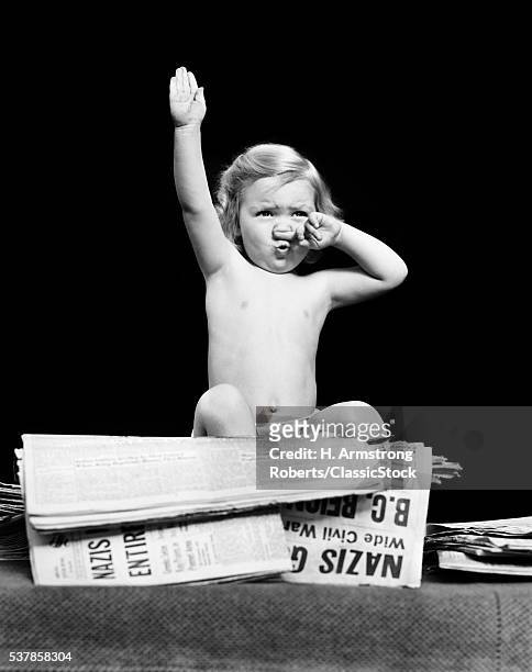 1940s LITTLE BLOND TODDLER GIRL IMITATING HITLER GIVING NAZI SALUTE SITTING ON PILE OF NEWSPAPERS