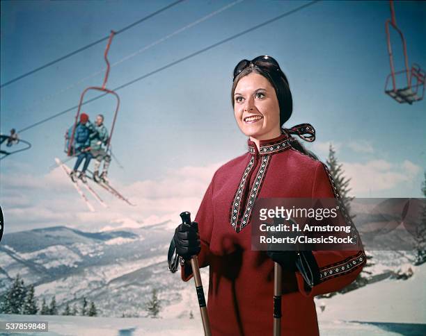 1970s WOMAN IN WINTER GEAR AND GOGGLES HOLDING SKI POLES SKI LIFT SNOW MOUNTAINS IN BACKGROUND