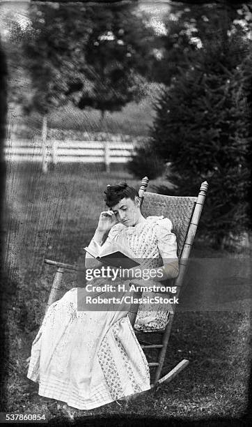1890s WOMAN SITTING IN ROCKING CHAIR IN BACKYARD READING BOOK