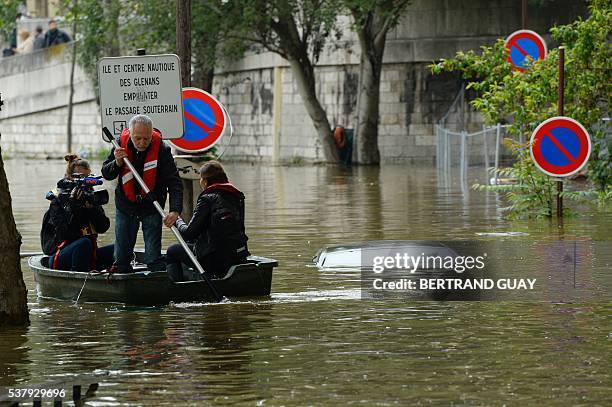 Journalists on a small boat pass near an immerged car in a flooded street along the quai Louis Bleriot in the 16th arrondissement in Paris on June 3,...