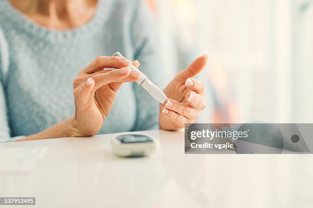 mature woman doing blood sugar test at home. - suiker stockfoto's en -beelden