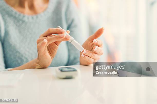 mulher madura dando análise de açúcar no sangue em casa. - diabetes imagens e fotografias de stock