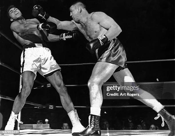 April 24, 1962--LOGAN ON ATTACK--George Logan bulls Cassius Clay into ropes and lands right during first round action at Sports Arena. This was...