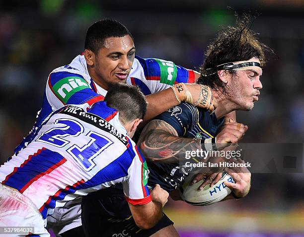 Ethan Lowe of the Cowboys is tackled by Jack Cogger and Pauli Pauli of the Knights during the round 13 NRL match between the North Queensland Cowboys...