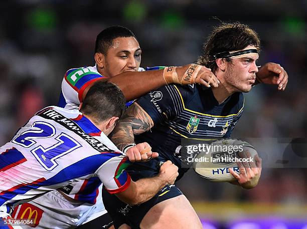 Ethan Lowe of the Cowboys is tackled by Jack Cogger and Pauli Pauli of the Knights during the round 13 NRL match between the North Queensland Cowboys...