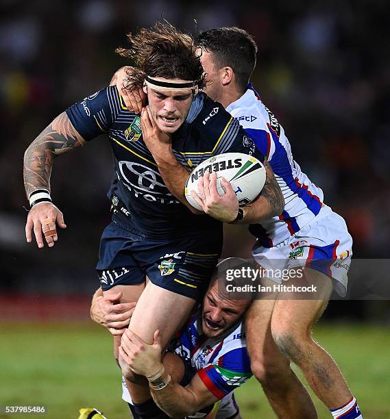 Ethan Lowe of the Cowboys is tackled by Jack Cogger and Nathan Ross of the Knights during the round 13 NRL match between the North Queensland Cowboys...