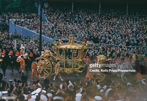 Queen Elizabeth II rides in the Gold State Coach past crowds of spectators on tiered viewing stands near Admiralty Arch and Trafalgar Square during...