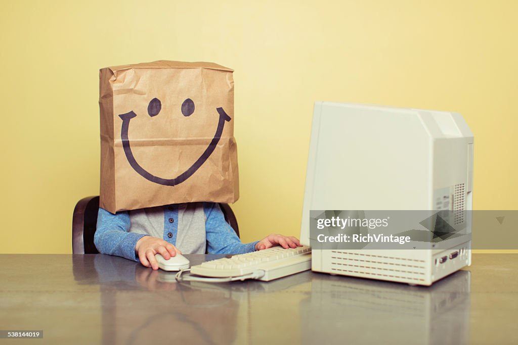 Young Boy at Computer with Paper Bag Smiley Face