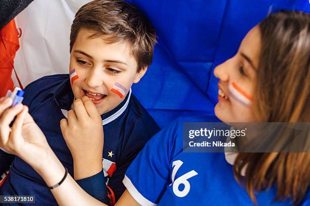 soccer fans preparations, painting face with tricolore - geschminkt gezicht stockfoto's en -beelden