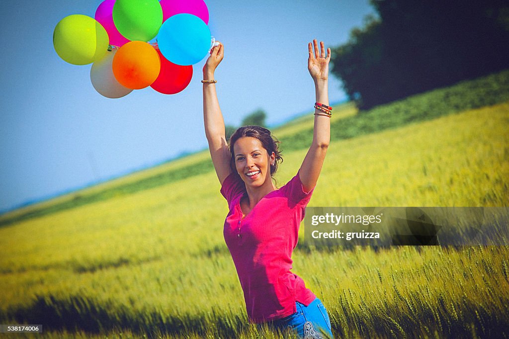 Cheerful woman holding colorful balloons, runs through wheat field