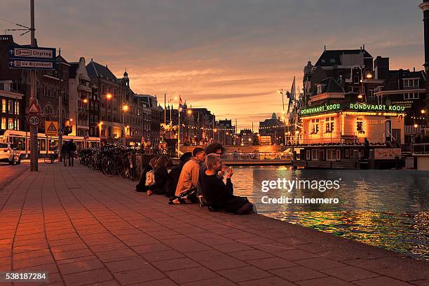 young people sitting canal at night - amsterdam sunset stock pictures, royalty-free photos & images