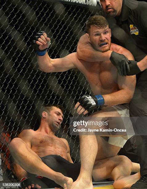 Referee Big John McCarthy pulls Michael Bisping off of opponent Luke Rockhold after knocking him out to win their Middleweight Title Bout at UFC 199...