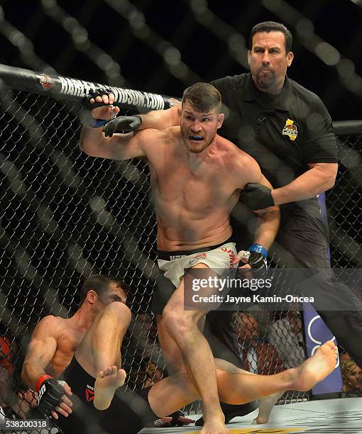 Referee Big John McCarthy pulls Michael Bisping off of opponent Luke Rockhold after knocking him out to win their Middleweight Title Bout at UFC 199...