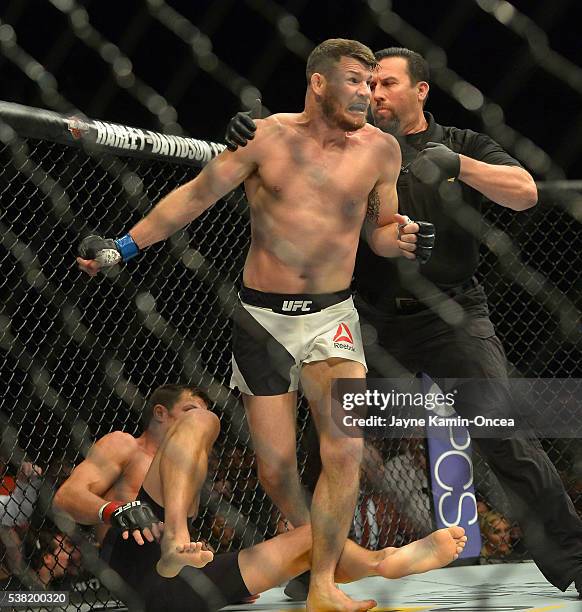 Referee Big John McCarthy pulls Michael Bisping off of opponent Luke Rockhold after knocking him out to win their Middleweight Title Bout at UFC 199...