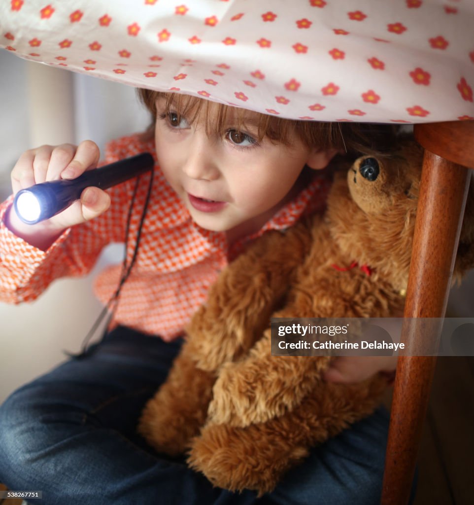 A boy playing with a lamp under a kitchen table