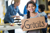 Young Hispanic girl holding GRACIAS sign at charity soup kitchen
