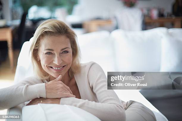 smiling mature woman on sofa - only mature women stock pictures, royalty-free photos & images