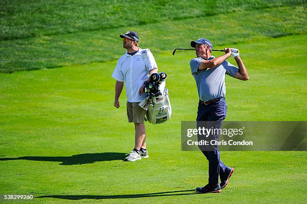 Matt Kuchar hits his approach shot on the 17th hole as caddie John Wood looks on during the final round of the Memorial Tournament presented by...