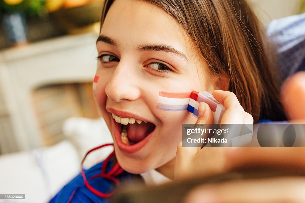 Français adolescente avec de la peinture sur visage tricolore et prenant un selfie