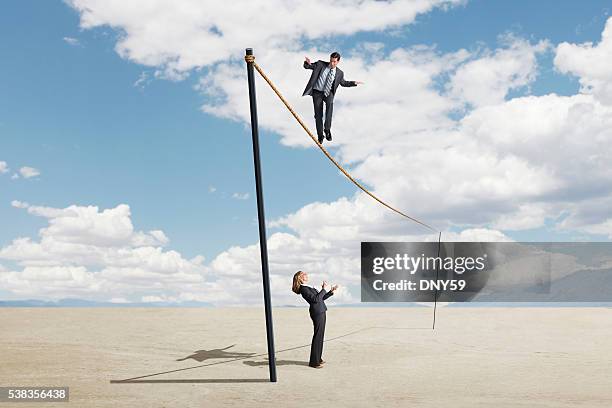 businessman walking tightrope as businesswoman nervously watches - woman tightrope stock pictures, royalty-free photos & images