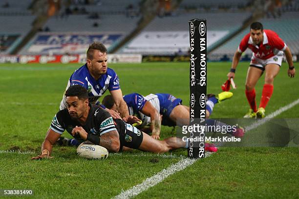 Ricky Leutele of the Sharks scores a try as he is tackled by Josh Reynolds and Sam Perrett of the Bulldogs during the round 13 NRL match between the...