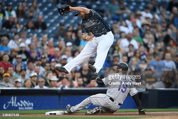 Brett Wallace of the San Diego Padres jumps for a high throw as Charlie Blackmon of the Colorado Rockies slides safely into third base during the...