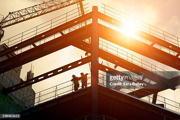 construction workers silhouetted against the sun - built structure foto e immagini stock