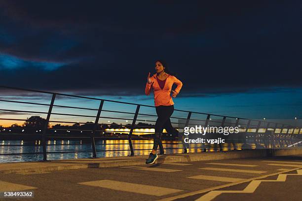 young woman jogging at night near river. - jogster stockfoto's en -beelden