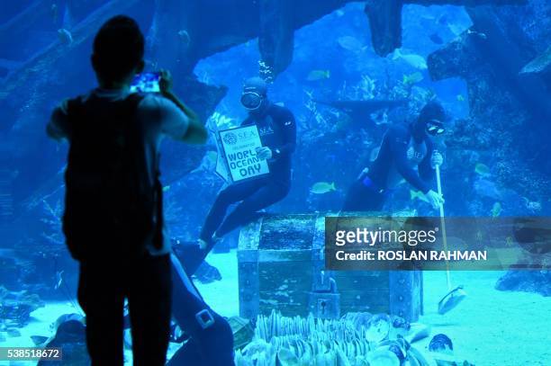 Two freedivers, one holding a sign that reads "World Ocean Day" and the other demonstrating cleaning the seabed at Resort World Sentosa's S.E.A...