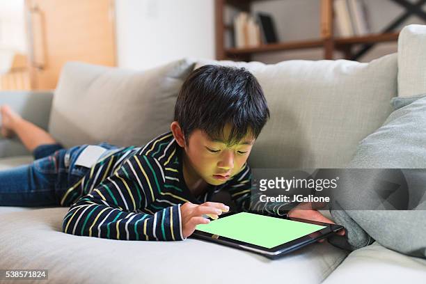 giovane ragazzo disteso su un divano con un compressa digitale giocando - ipad glow foto e immagini stock