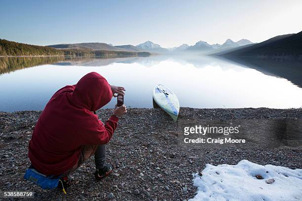 a man takes a photograph while stand up paddle boarding (sup) on a calm lake mcdonald in glacier national park. - solo un uomo foto e immagini stock